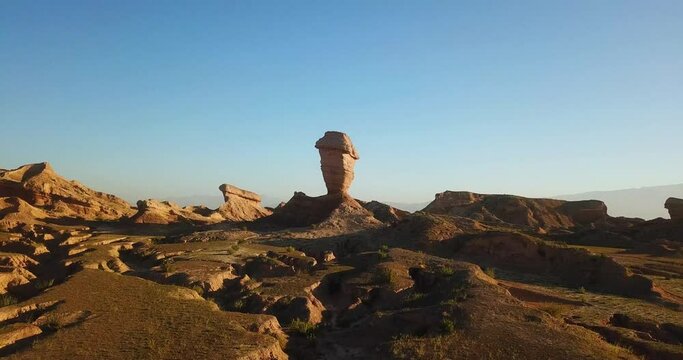 Fly over a single alone pillar wind erosion rock cliff geology erosion in desert climate in Iran natural wonderful scenic landscape in summer sunset time blue sky and wild nature road trip in Iran