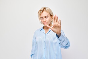 Blonde woman showing stop gesture with hand, signaling boundaries or denial, on light background.