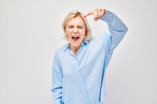 Woman gesturing "loser" sign on forehead, expressing playful mockery or self-deprecating humor, isolated on light background.