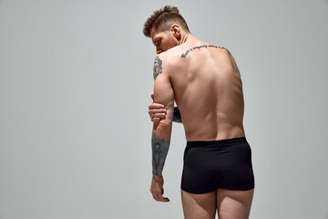 Banner. Tattooed attractive man in underwear man holds his hand on his elbow against grey studio...