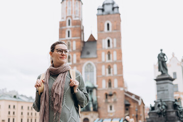 Tourist happy woman in glasses on Market Square in Krakow, Traveling Europe in autumn. St. Marys Basilica, cloudy day