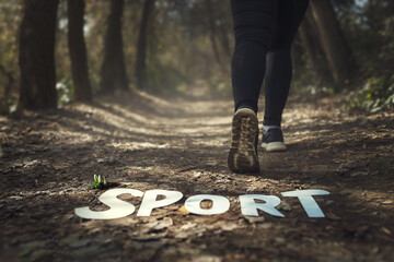 A close-up of a jogger's feet on a forest trail with the word 'SPORT' laid out on the ground, symbolizing an active lifestyle and outdoor exercise. The focus on the runner's shoes highlights the impor - obrazy, fototapety, plakaty
