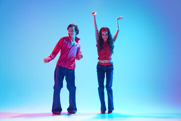 Rock and roll era. Elegant stylish young couple dancing retro dance against blue background in neon...