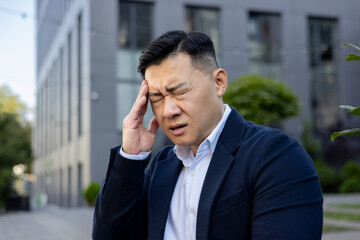 Stressed businessman with headache standing outdoors