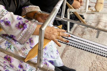 Hands of an old Emirati woman using traditional weaving machine