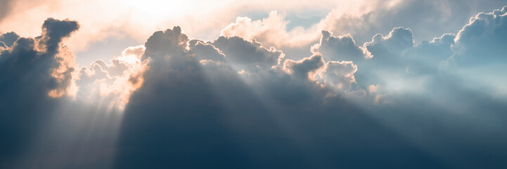 Beautiful sky background with clouds and sunbeams. Dramatic cloudscape with sun rays. Bright sunshine and sunny glow. Wide panoramic background for design.
