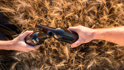 Two hands clink bottles of beer on a background of a wheat. Topview
