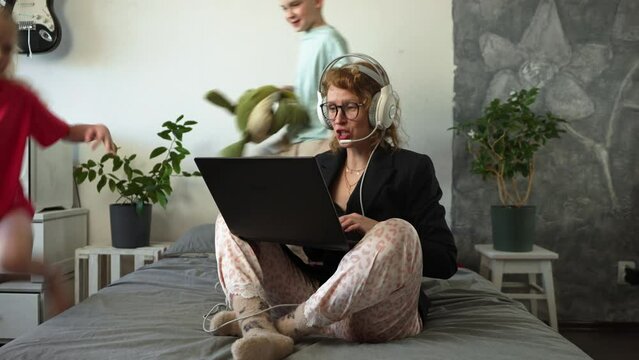 Remote work at home: A girl in a jacket and pajamas, a call worker contacts a client via video conference. Children run around, make loud noises and get in the way.
