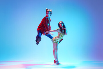 Dynamic image of young artistic couple dancing retro dance, performing against blue background in...