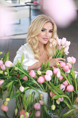 Obraz na płótnie Canvas A beautiful happy smiling woman with blond hair stands near a white bathtub full of flowers.