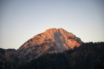 Blick auf einen golden leuchtenden Berggipfel mit umgebenden Wald in der Morgenstunde