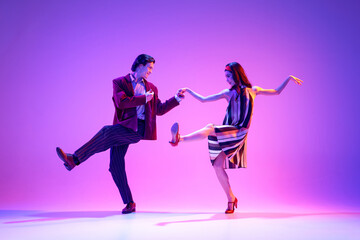 Fototapeta na wymiar Young man and woman in stylish clothes dancing retro dance, boogie woogie against purple background in neon light. Concept of hobby, dance class, party, 50s, 60s culture, youth