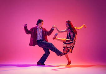Stylish, beautiful young couple, man and woman in retro clothes dancing swing against pink...
