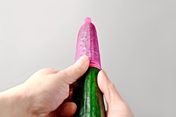 Unrecognizable person  Pulls a red condom over a cucumber.. Safe sex concept.	