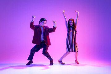 Artistic young man and woman in retro style clothes dancing boogie woogie against purple background...