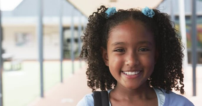 Biracial girl with curly hair smiles at school, wearing blue hair ties, with copy space