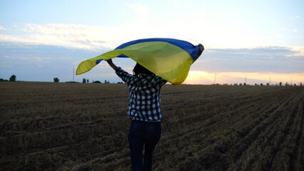 Ukrainian woman running with raised flag Ukraine above her head on wheat field at sunset. Lady jogging with national blue-yellow banner on barley meadow at sunrise. Victory against russian aggression. - 757183853