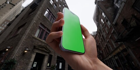 Hand holding a smartphone with a green screen on an urban city street background - 757184259