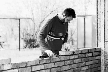 a man builds a wall of bricks, lays a brick on a cement sand mortar black white photo