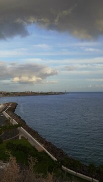The coast of Pasito Blanco in the Canary Islands with calm ocean and the Faro de Maspalomas on background