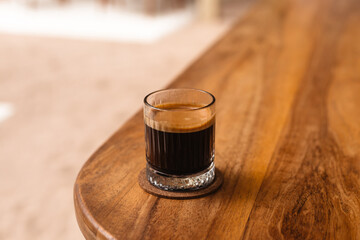 Black coffee in a glass on a wooden table side view
