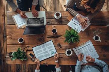 A diverse group of individuals sitting around a table, engaged in various activities on their laptops, Overhead view of a professional meeting with documents and coffee cups, AI Generated - obrazy, fototapety, plakaty