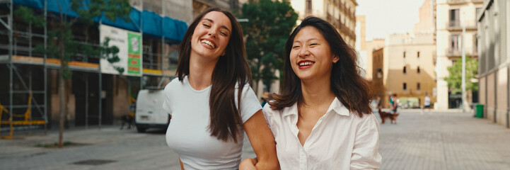 Young multiethnic women walk laughing down the street on warm summer day on the old town...