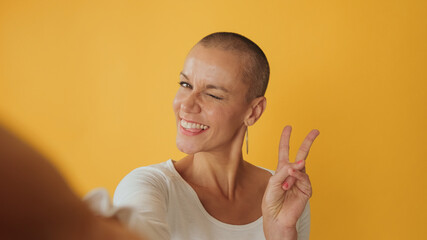 Close-up, young hairless woman taking selfie shows fingers victory gesture at camera, isolated on...