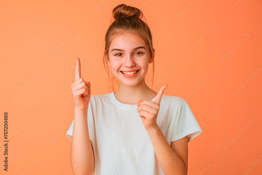 Wall mural Portrait of a young girl points her finger to the side on a peach background. Copy space