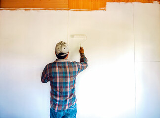 Back view of Workers painter are painting the wooden walls of the room white with paint roller,improvement home interior concept.