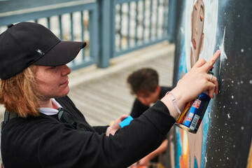 Female artist in black cap is painting picture with paint spray can spraying it onto canvas at...