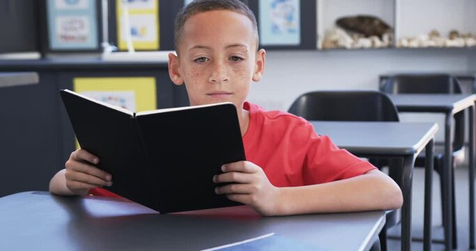 Biracial boy with freckles is reading a book in a classroom at school