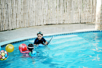 A little asian boy and girl in swimming in the pool. Cute girl playing in outdoor swimming pool on a hot summer day. Kids learn to swim.