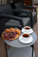 breakfast on the terrace, black tea, grapes and croissants. aesthetic breakfast on the street. two white cups with tea. country recreation. rest and relaxation