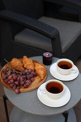 breakfast on the terrace, black tea, grapes and croissants. aesthetic breakfast on the street. two white cups with tea. country recreation. rest and relaxation