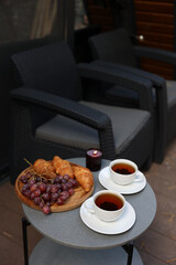 breakfast on the terrace, black tea, grapes and croissants. aesthetic breakfast on the street. two white cups with tea. country recreation. rest and relaxation