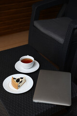 breakfast on the terrace, black tea, and cheesecake and a laptop. aesthetic breakfast on the street. white cup with tea. country recreation. rest and relaxation. working on a laptop and drinking tea.