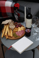 Fototapeta na wymiar rest and relaxation. red wine, glasses, book, candles and snacks are on the table. romantic dinner on the terrace. aesthetic photo. wooden board with grapes, cheese, sausage, olives and grisini