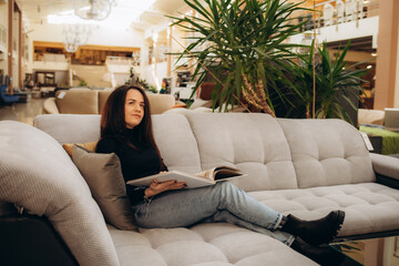 a woman looks at a catalog of sofas while sitting in a furniture store