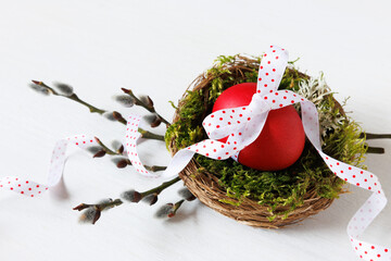 Easter card. Nest with a painted red egg with a ribbon in the nest and willow branches on a white wooden background. - 757215651