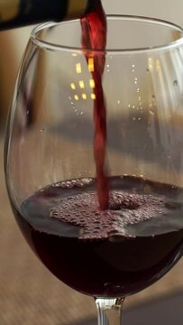 Close up of hand pours dry red wine from bottle into glass in restaurant. French wine. Drink. Vertical shot