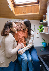 Boy with his two mothers giving him a kiss in the kitchen of their house