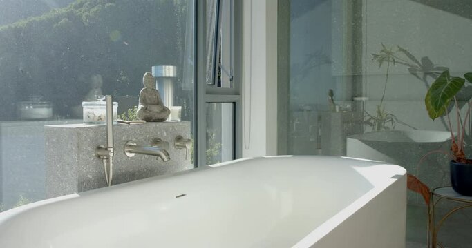 A serene bathroom with a white bathtub is bathed in natural light from a large window