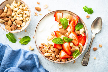 Yogurt with granola, nuts and strawberries on white. Healthy snack or breakfast, fruit salad. Top...