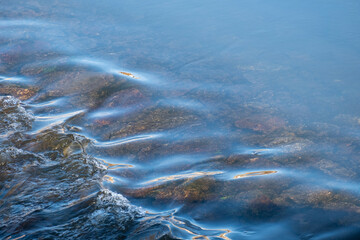 Detail of the fresh, transparent water flowing over the rocks in the background and forming small waves.