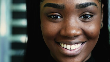 One happy young black teen girl smiling at camera in detail macro close-up, looking directly at...