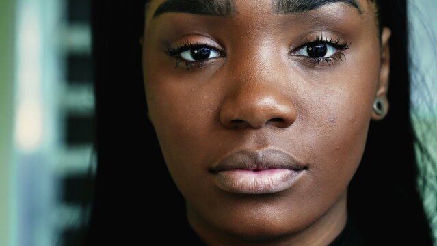 Macro close-up portrait of a serious young black woman looking directly at camera with solemn expression. South American hispanic adult girl in 20s of African descent