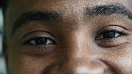 Macro closeup eyes of a young happy black man smiling at camera, facial features detail of person...