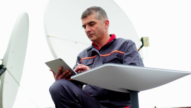 Telecommunication internet connection concept, industrial production station concept. Television worker, engineer, technician sets up an innovative satellite dish for the Internet.