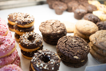 Various colorful donuts, cookies on the shelf in showcase on display at in the coffee shop, in bakery shop. Various bread type, sweet foods, trendy cafe